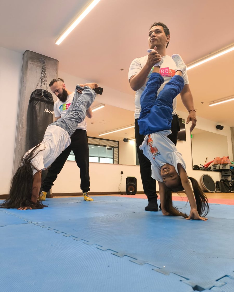 Instructores de Brinca Playing acompañando a niñas en paradas de manos durante una clase de capoeira y gimnasia