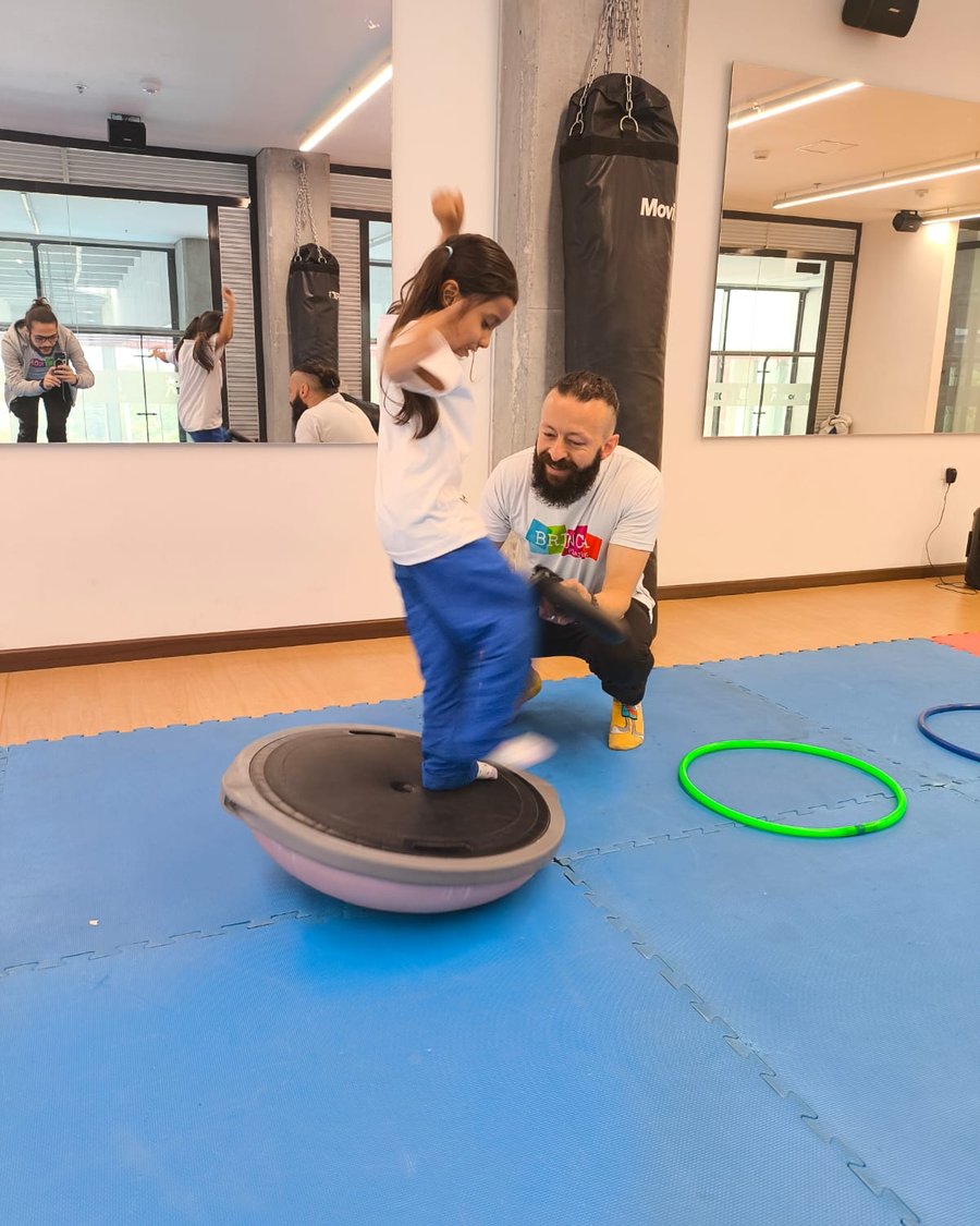 Niña saltando sobre una plataforma de equilibrio junto a un instructor de Brinca Playing